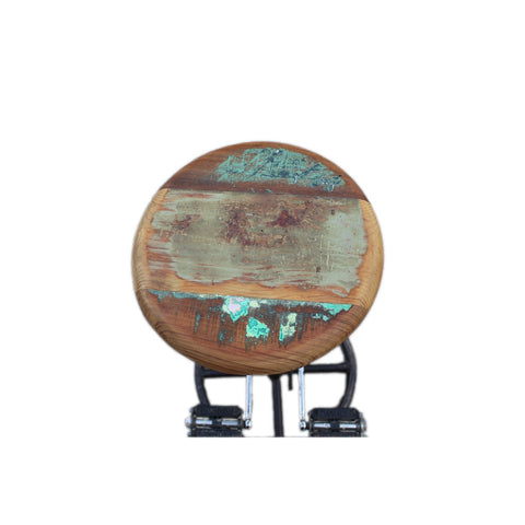 The Industrial Barstool Patina features a round reclaimed wood seat with faded green and brown paint patches, distressed for a weathered look, and is supported by black metal legs. Shown photographed against a plain white background.