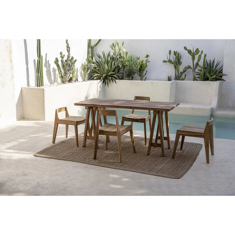 Five Paxi Dining Chairs in Natural for outdoor use surround a wooden dining table set on a woven rug by the pool, amidst cacti and succulents against a white wall.