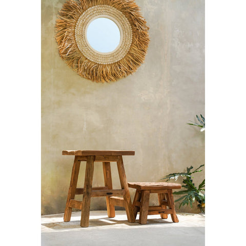Rustic wooden stool set against a textured wall with a round woven mirror.
