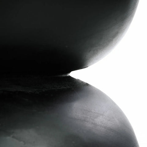 Close-up of two smooth, dark, rounded objects—resembling black suar wood—stacked on top of each other, with a small gap between them and a bright white background.
