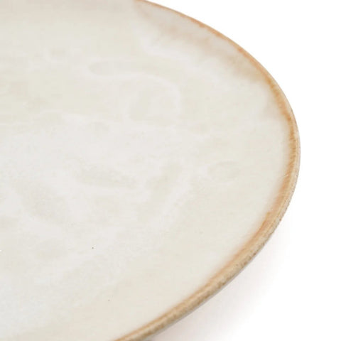 A close-up of the edge of a ceramic plate with a smooth, off-white, slightly marbled surface and a thin, light brown rim—showcasing the allure of handmade tableware inspired by Portuguese ceramics.