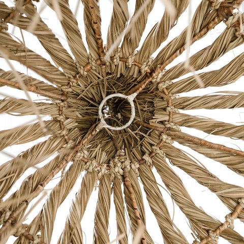 Close-up view from below of The Guagua Pendant - Natural - L, a handmade lamp crafted from natural straw with concentric circular patterns and textured strands radiating outward.