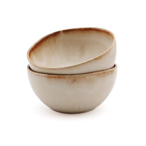 Two handmade tableware ceramic bowls with uneven rims are stacked together. Off-white with a light brown, rustic edge, these Portuguese ceramics sit on a plain white background.