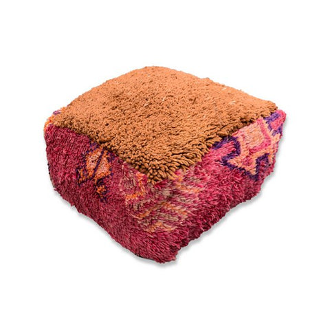 The Moroccan Floor Cushion features a square, textured design with a shaggy rust-orange top and patterned pink and purple sides, evoking vintage Berber rugs. Shown on a white background.