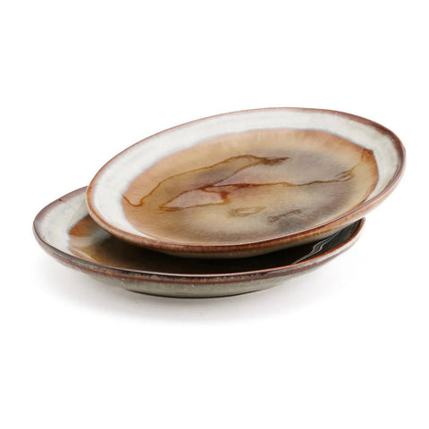 Two ceramic plates with earthy brown, tan, and cream tones stacked slightly askew on a white background. The plates feature a glossy, marbled finish and irregular edges, showcasing the unique charm of handmade tableware.