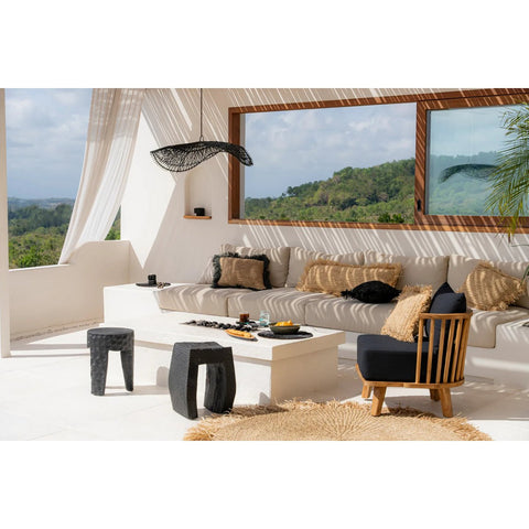 A bright, modern outdoor space with a beige sectional, black and tan cushions, white coffee table, black stools, round woven rug, and large windows overlooks green hills. The Chapeau Pendant - Black - L adds warmth above sheer-curtained elegance.