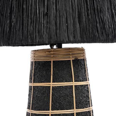 Close-up of The Naxos Table Lamp - Black Natural, featuring a textured black base with a grid of light-colored bamboo strips and a matching black lampshade. The rattan-inspired design stands out against the white background.