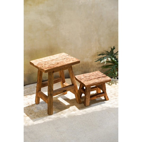 Wooden step stool and small side table against a beige wall with a plant in the corner.