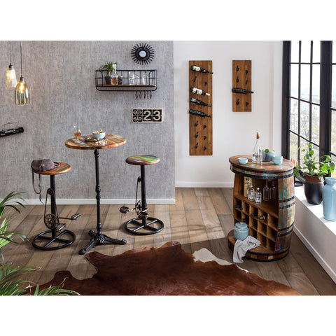 A modern rustic bar area featuring three tall tables, a curved bar cabinet, Industrial Barstool Patina stools, wall-mounted wine racks, hanging lights, plants, and decor on wood flooring with a cowhide rug.