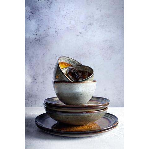 A stack of handmade tableware, including plates and bowls in earthy tones of brown and gray, arranged neatly against a textured light gray background.