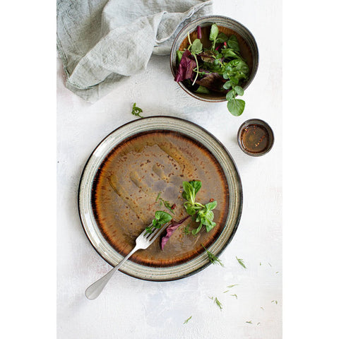 The Comporta Dinner Plate - L (Set of 4) showcases fresh salad greens with a fork, paired with a bowl, dressing cup, and gray napkin. The handmade plates bring rustic charm to this minimal white table setting.