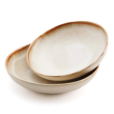 Two shallow, round ceramic bowls with a light cream glaze and a brown rim, stacked slightly askew against a white background—beautiful examples of chip-proof handmade tableware.
