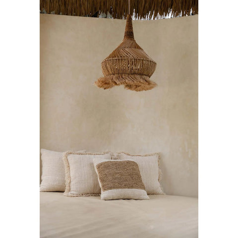 A cozy seating area with cream-colored pillows and a woven, dome-shaped rattan pendant light hanging from the ceiling against a neutral beige wall.