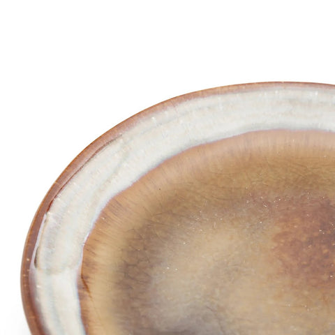 Close-up of the edge of a ceramic plate with a brown and beige crackle glaze finish, showing a textured and slightly uneven rim against a white background—an elegant example of handmade tableware.