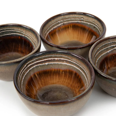 Four ceramic bowls with glossy brown and tan gradient glaze, featuring concentric rings and an earthy, handmade tableware look, are grouped closely together on a white background.