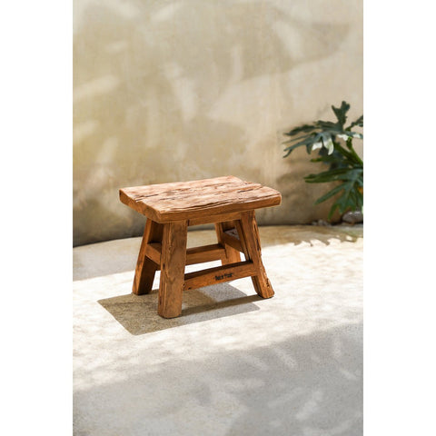 Rustic wooden stool on a textured surface with a plant in the background