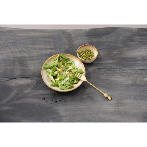A bowl of green salad with a gold fork beside it, served in chip-proof handmade tableware, and a smaller bowl of capers on a gray wooden surface.