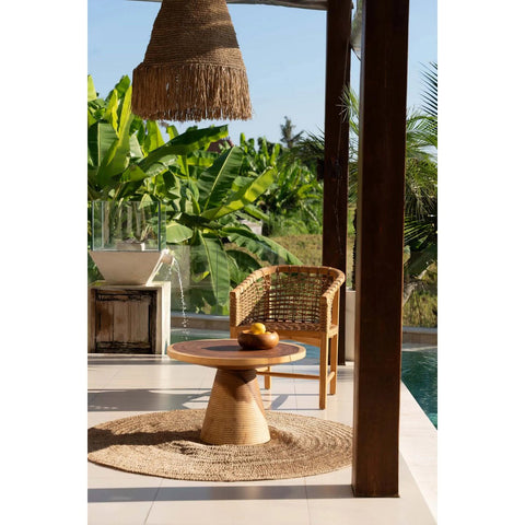 Outdoor setting with a wicker chair and table near a pool, surrounded by greenery.