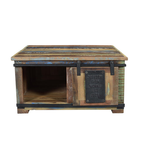 The Chest Coffee Table Patina is a rustic piece made from recycled wood, showcasing multicolored panels, a barn-style sliding door with "Jupiter Iron Works Est 1953," and an open storage compartment.