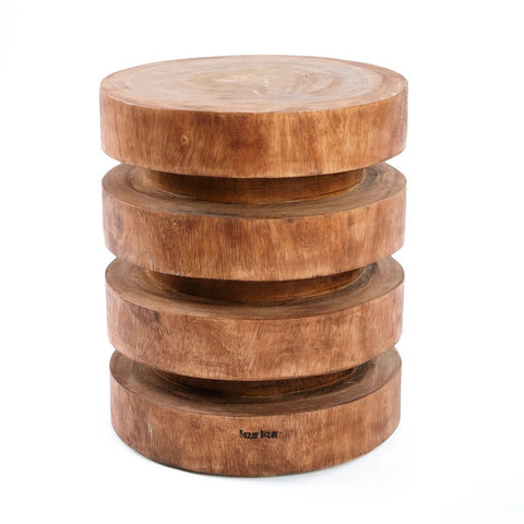 The Massaka Stool - Natural features a round, carved wooden form with a stacked, layered design and visible wood grain, shown against a white background.