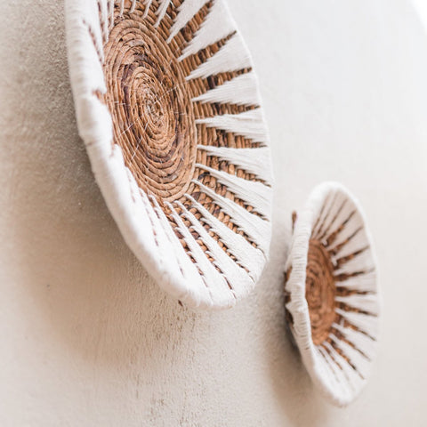 Two Decorative Bowl MADALA baskets, crafted from banana fibre with white and natural brown patterns, hang at an angle on a light wall, creating a simple and modern boho-inspired wall decoration.