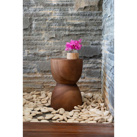 Wooden side table with a pink flower against a stone wall.