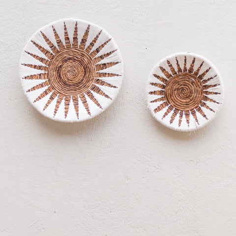 Two round Decorative Bowl MADALA banana fibre baskets with spiral centers and radiant brown and white sunburst patterns make stunning boho wall decor. The larger left basket adds depth to this natural display on a light-textured wall.