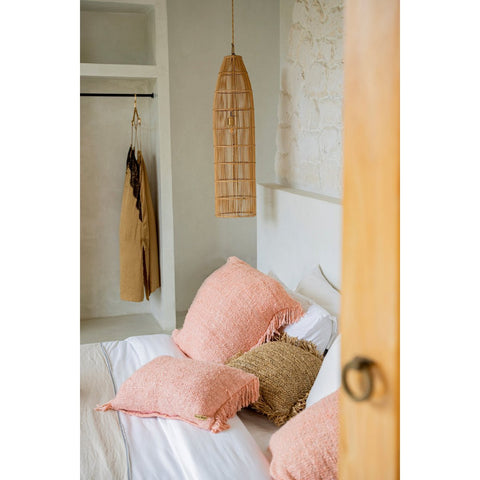 A cozy bedroom features a white bed with pink and beige textured pillows, a light stone wall, an open closet with a hanging tan robe, and The Fish Trap Pendant - Natural - L overhead for a soft, natural aesthetic.