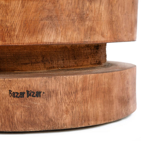 Close-up of The Massaka Stool - Natural: a carved wooden stool with two stacked circular sections and visible wood grain. “Bazar Bizar” is printed in black, emphasizing its authentic natural wood furniture appeal.