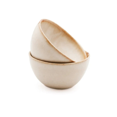 Two off-white ceramic bowls, crafted from Portuguese ceramics with a smooth matte finish, are stacked together against a white background. The top bowl is slightly tilted, resting inside the chip-proof bottom bowl.
