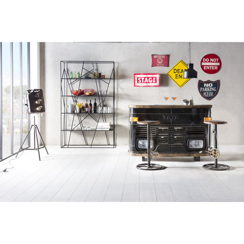A modern loft bar area includes a metal bar, the Industrial Barstool Patina, a geometric drinks shelf, vintage road signs on the wall, and a studio light by large windows with a city view.