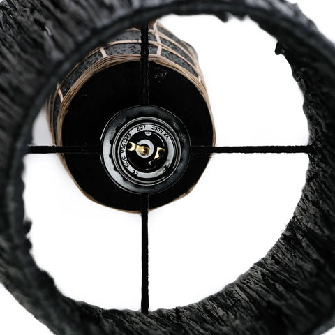 Close-up of the inside of The Naxos Table Lamp - Black Natural, highlighting the black cylindrical shade, central light bulb socket, and intersecting metal rods forming a cross pattern.