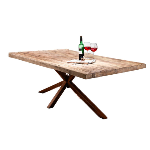 The Woodz Table 240x100 cm features a rustic industrial design with angled metal legs and a solid wood top, displaying a wine bottle, two filled glasses, and a folded napkin against a plain white background.