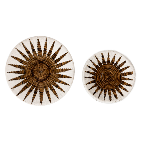 Two round Decorative Bowl MADALA baskets, crafted from banana fibre with brown and natural sunburst designs, make striking boho wall decor. Pictured on a white background, the left bowl is larger than the right.