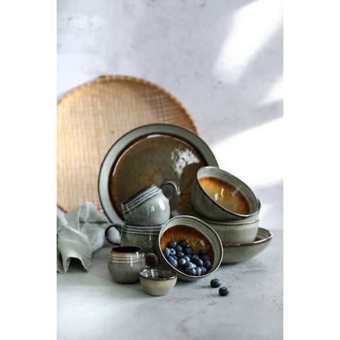A set of four rustic, handmade Comporta Pasta Plates is arranged on a light surface, one holding fresh blueberries. A woven placemat and folded cloth napkin complete the soft natural look.