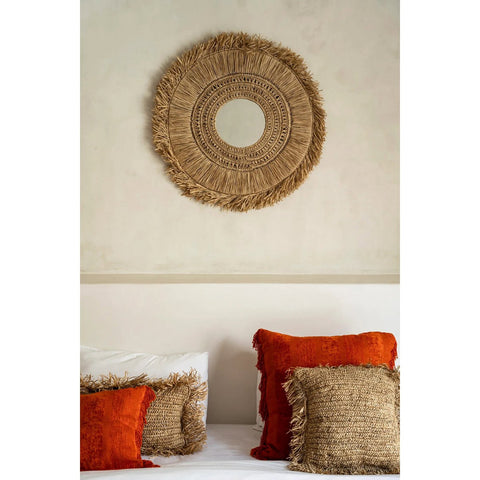 Decorative wall mirror with raffia design above a bed with matching pillows.
