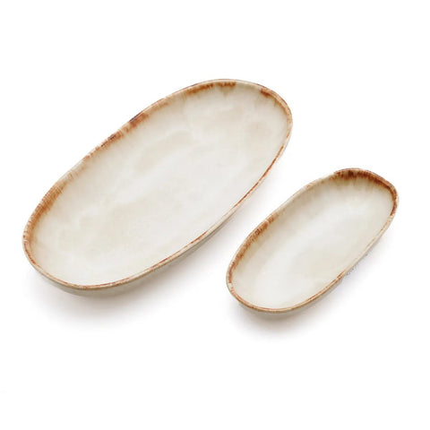 Two oval ceramic serving dishes with slightly uneven rims and a white glaze, featuring light brown edges. Inspired by Portuguese ceramics, one dish is larger than the other, and both are placed on a white background.