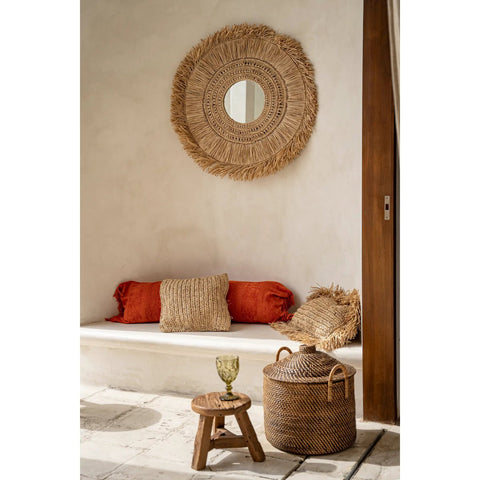 Decorative wicker mirror on a wall above a seating area with cushions and a small table.