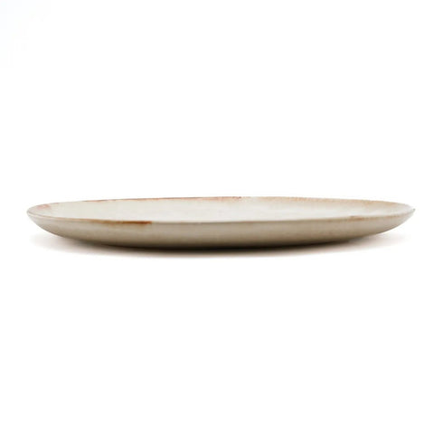A side view of a simple, round, beige ceramic plate with a slightly raised edge, expertly crafted as handmade tableware and set against a plain white background.