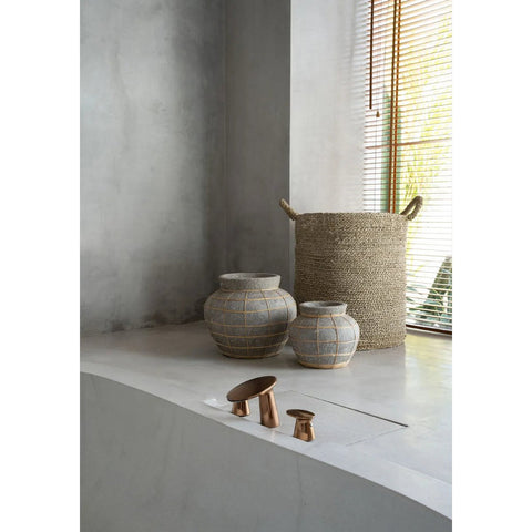 Woven baskets and ceramic pots on a concrete floor with a window in the background