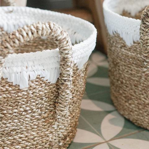 Two Round Seagrass Baskets WAIGEO with sturdy handles and white trim rest on a green and white tiled floor. Crafted from natural fibers, these handmade baskets offer rustic style and textured charm.