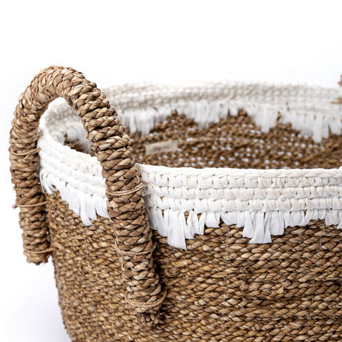 A close-up of the Round Seagrass Baskets WAIGEO, handmade with natural brown fibers, two handles, and a decorative white woven band with fringe around the top edge. The background is plain white.