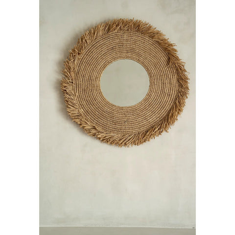 Round woven mirror with frayed edge on a plain wall
