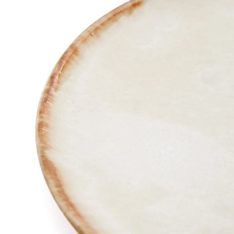A close-up of the rim of a ceramic plate, featuring a beige, slightly glossy surface with a brown, rustic edge. The handmade tableware has a subtle texture, minimalist design, and draws inspiration from Portuguese ceramics.