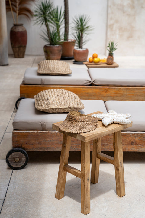 A serene outdoor scene features wooden lounge chairs with cushions and wicker accents. A wooden stool holds a woven hat. Potted plants and a small bowl of oranges add a touch of greenery and color.