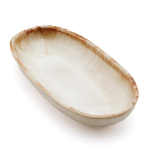 A shallow, oval ceramic dish with a slightly textured, off-white surface and a light brown, uneven rim, this piece of handmade tableware reflects the charm of Portuguese ceramics, set against a crisp white background.
