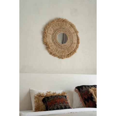 Round woven mirror on a wall above a bed with patterned pillows.