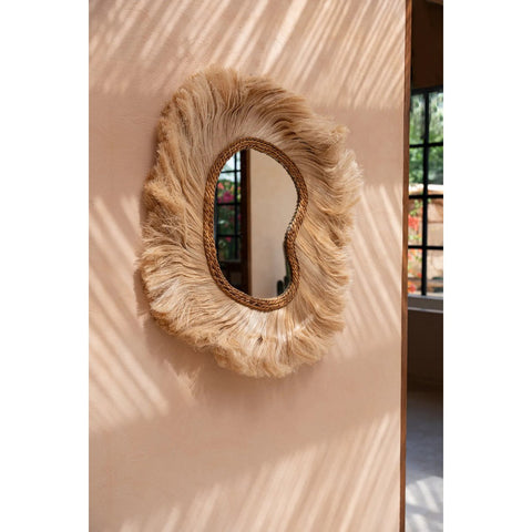 Decorative wall mirror with raffia fringes on a light pink wall
