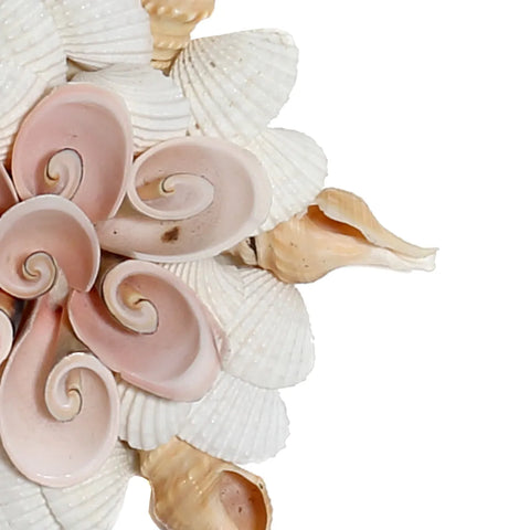 A decorative arrangement of white and pink seashells forms a flower-like pattern, with spiraled shells in the center and layered petals made from scallop shells. This bohemian decoration, handmade by Indonesian craftsmen, is set against a plain white background.