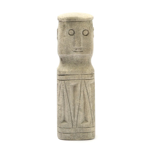 A hand-carved sandstone sculpture with a cylindrical body and a simplistic human face features two round eyes and a straight mouth. Reminiscent of creations from traditional villages, the Sumba Stone-inspired piece is adorned with linear, geometric carvings.